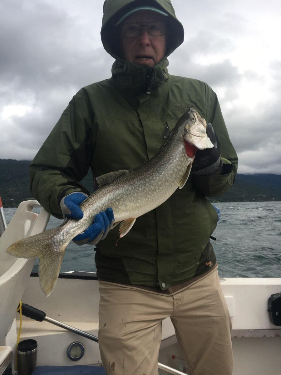 A man in a green jacket is holding a fish on a boat