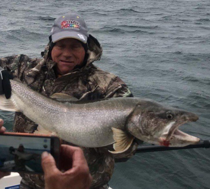 A man on a boat holding a large fish with the word fishing on his hat