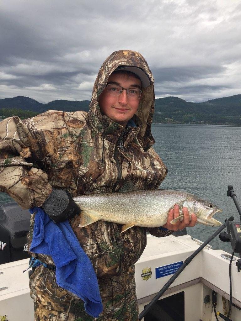 A man in a camouflage jacket is holding a large fish on a boat.