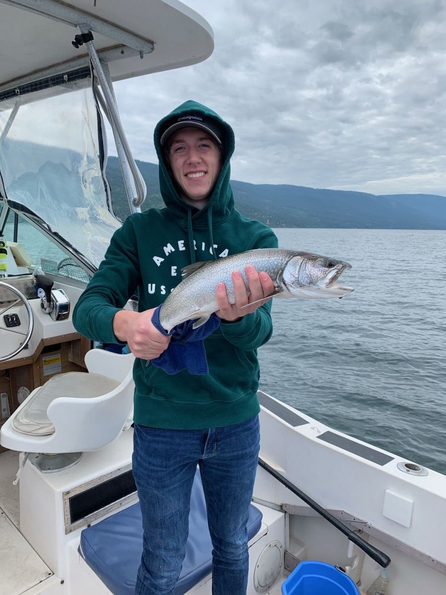 A man in a green hoodie is holding a fish on a boat.