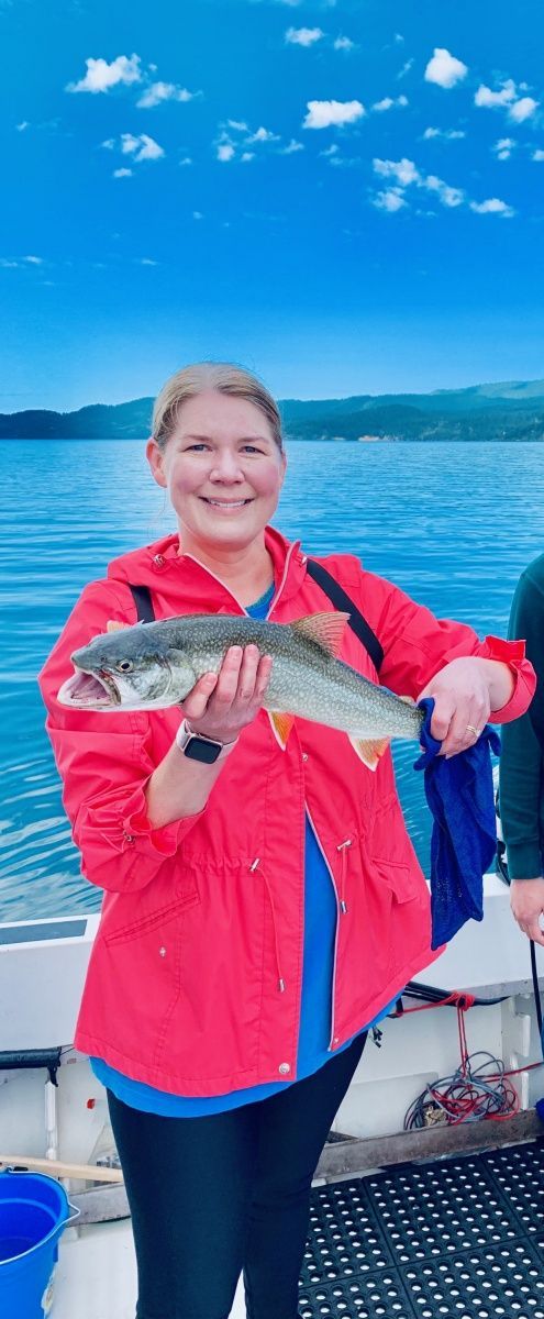 A woman in a red jacket is holding a fish on a boat.
