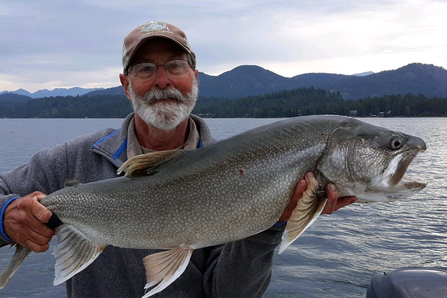 A man is holding a large fish in his hands in front of a lake.
