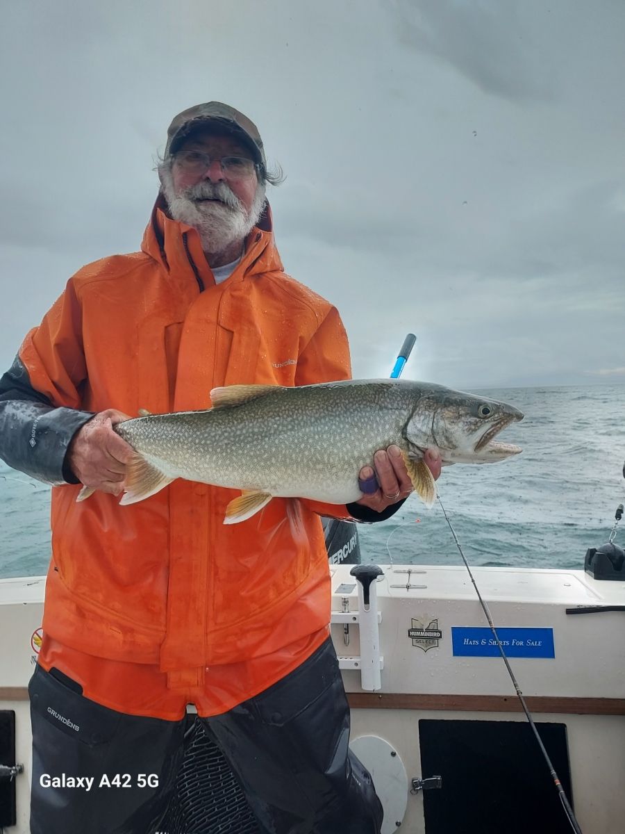 A man in an orange jacket is holding a large fish on a boat.