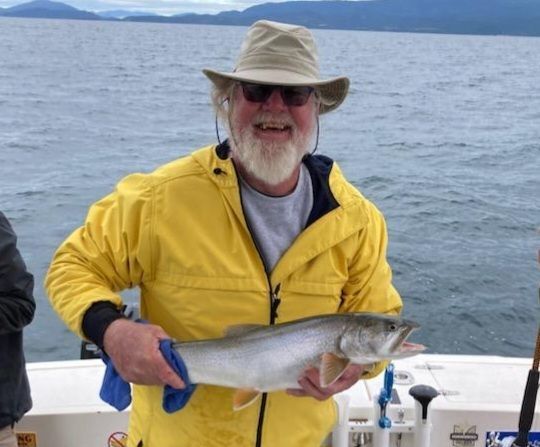 A man in a yellow jacket is holding a large fish
