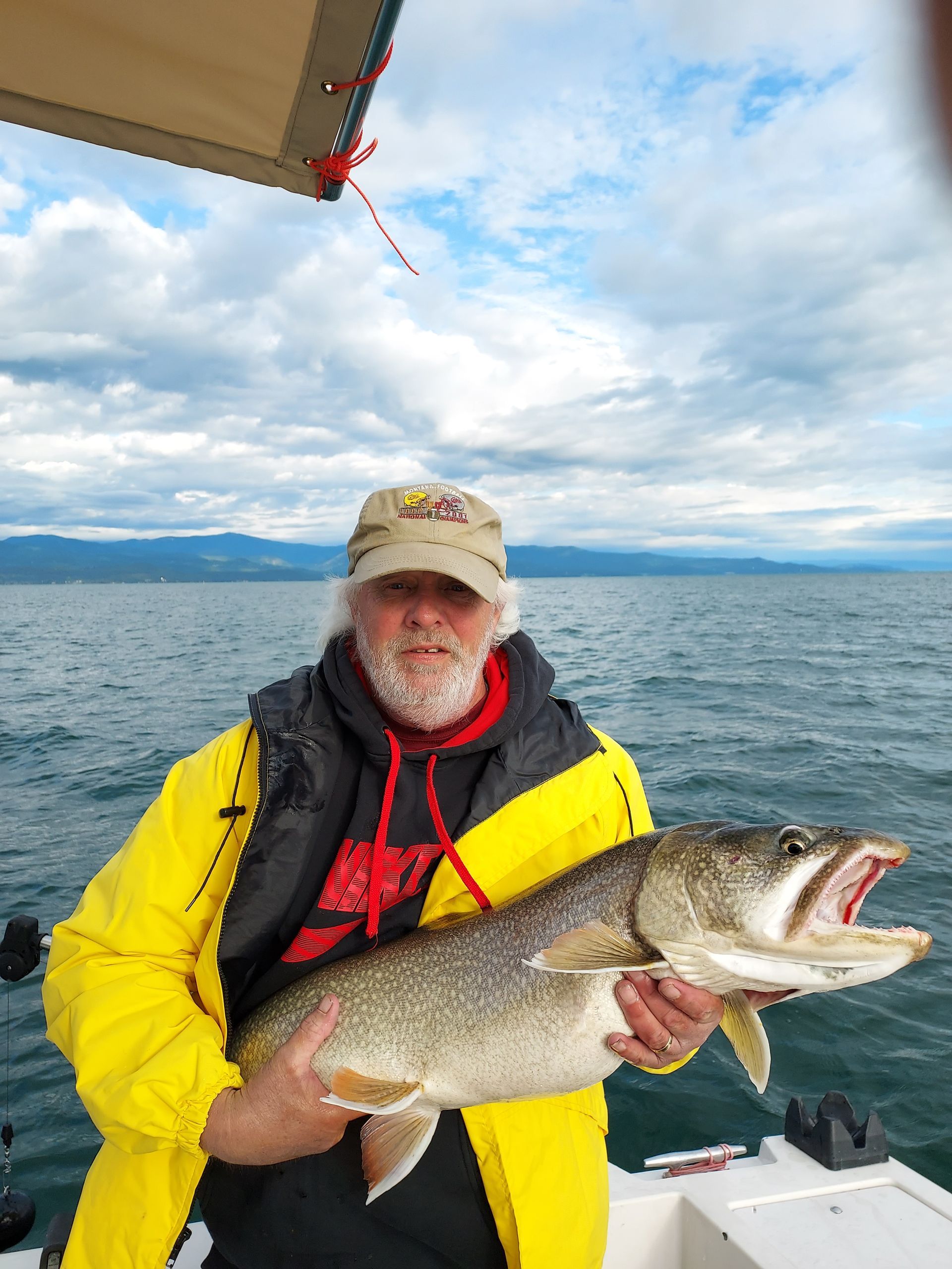 A man in a yellow jacket is holding a large fish on a boat.