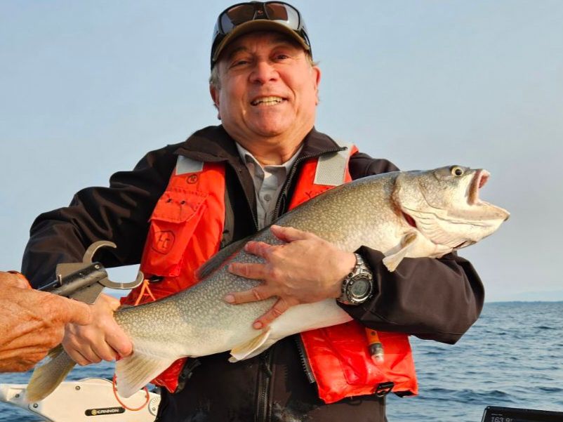 A man in an orange vest is holding a large fish in his hands.