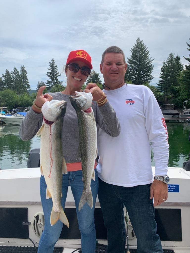 A man and a woman are holding two fish on a boat.