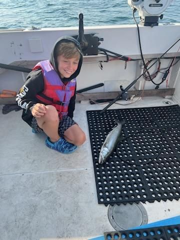 A young boy is kneeling on the deck of a boat next to a fish.