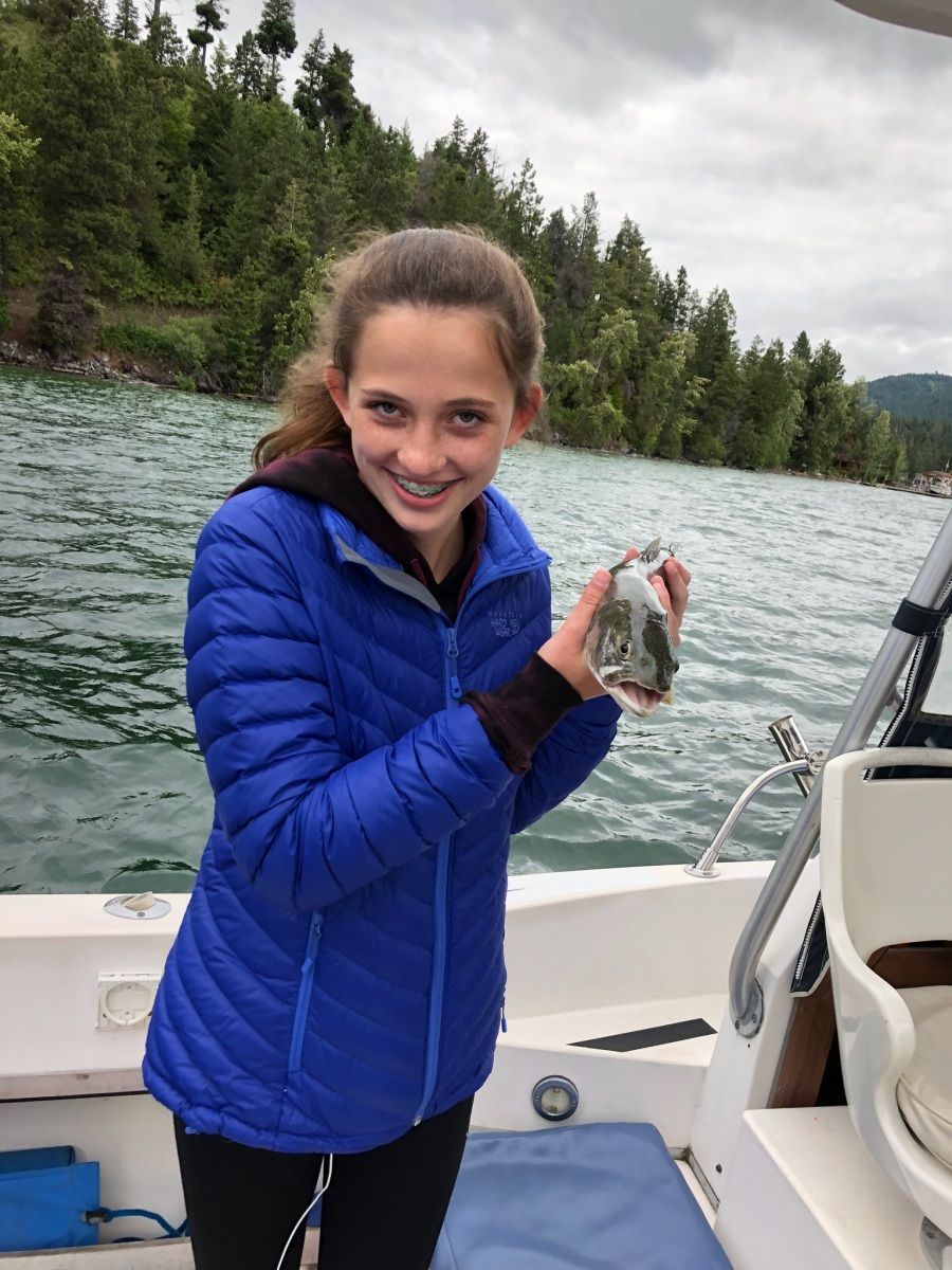 A young girl in a blue jacket is standing on a boat holding a fish.
