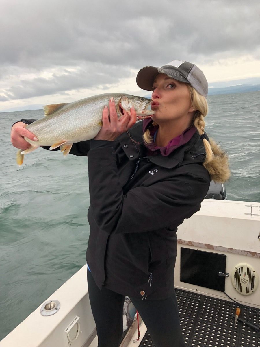A woman is holding a large fish in her hands and kissing it.