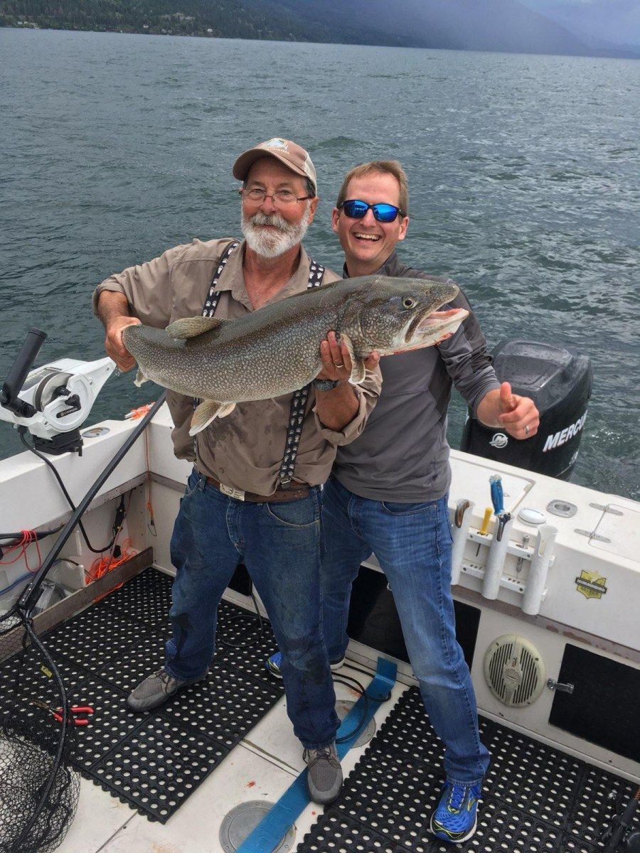 Two men are standing on a boat holding a large fish.
