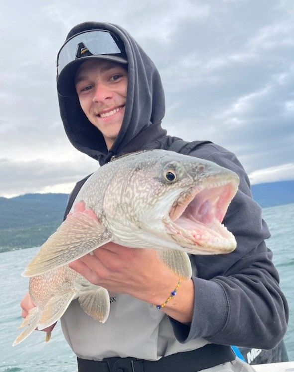 A man in a hoodie is holding a large fish in his hands.