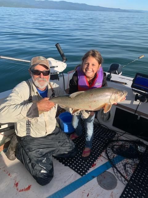 A man and a girl are kneeling on a boat holding a fish.
