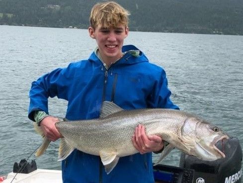 A young man in a blue jacket is holding a large fish in his hands.