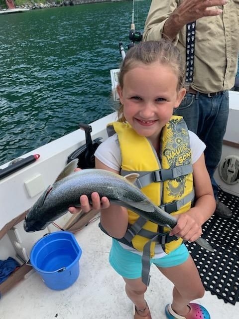 A little girl wearing a life vest is holding a fish