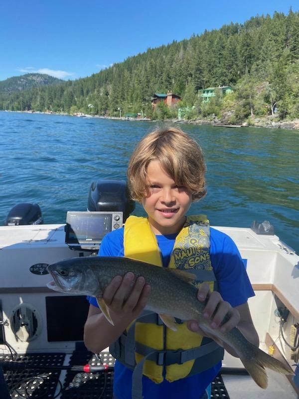 A boy wearing a life vest is holding a fish on a boat