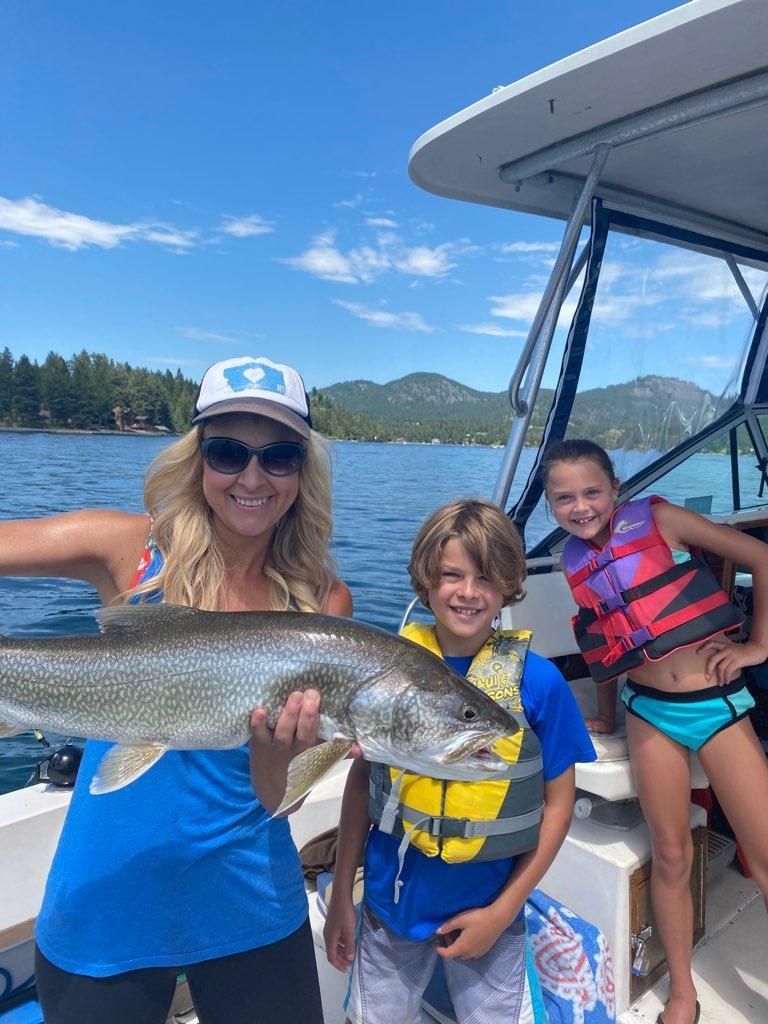 A woman is holding a large fish on a boat with two children.