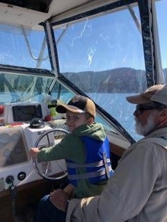 A man and a boy are sitting on a boat . the boy is wearing a life jacket.