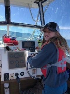 A young girl is sitting at the steering wheel of a boat.