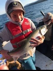 A young boy in a life jacket is holding a fish on a boat.