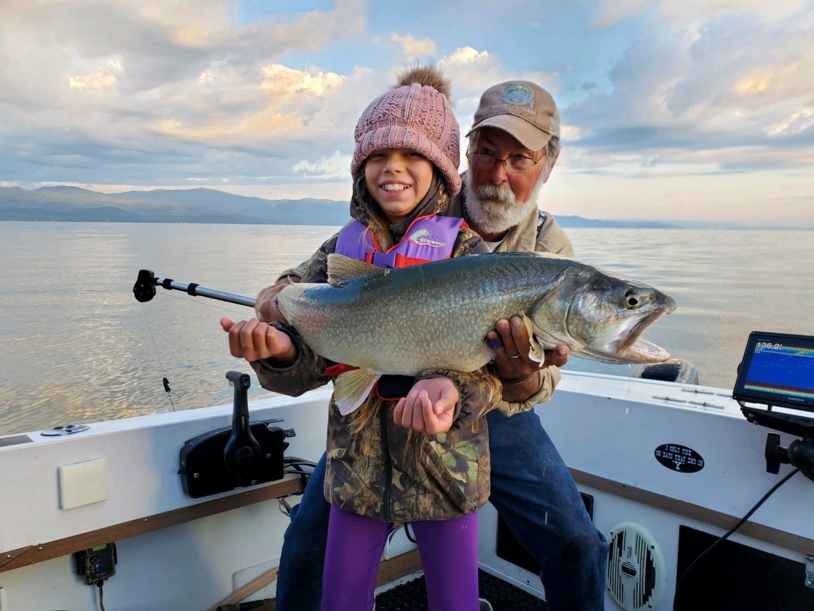 A man and a little girl are holding a large fish on a boat.
