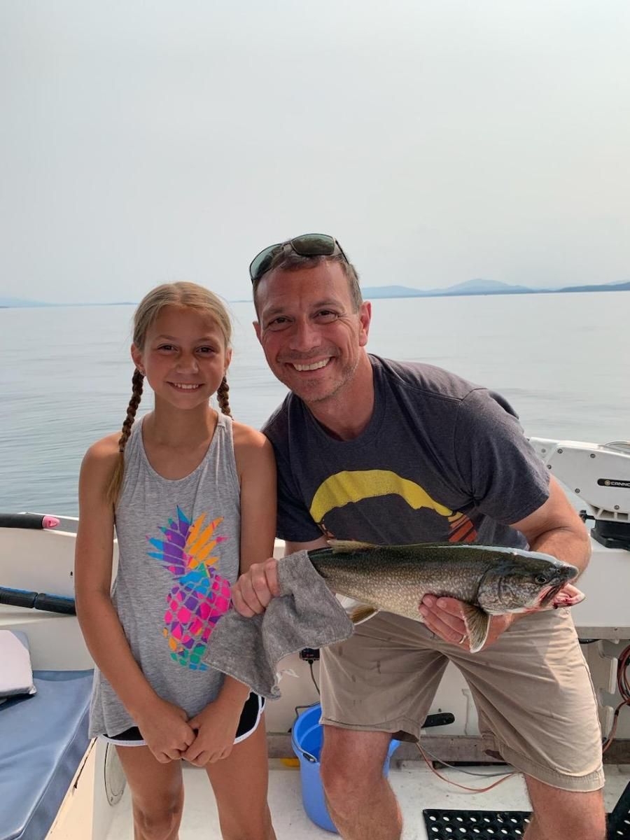 A man and a girl are standing on a boat holding a fish.