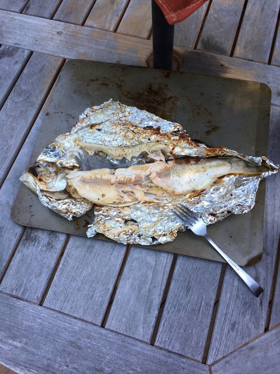 A piece of fish wrapped in tin foil with a fork on a wooden table