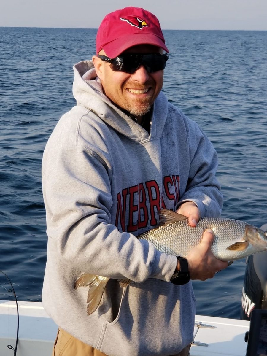 A man wearing a nebraska sweatshirt is holding a fish