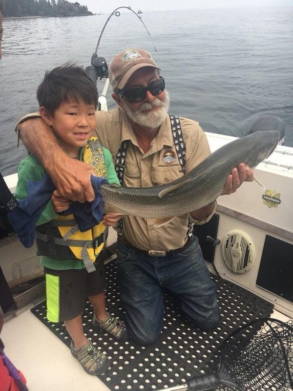 A man and a boy are kneeling on a boat holding a fish.