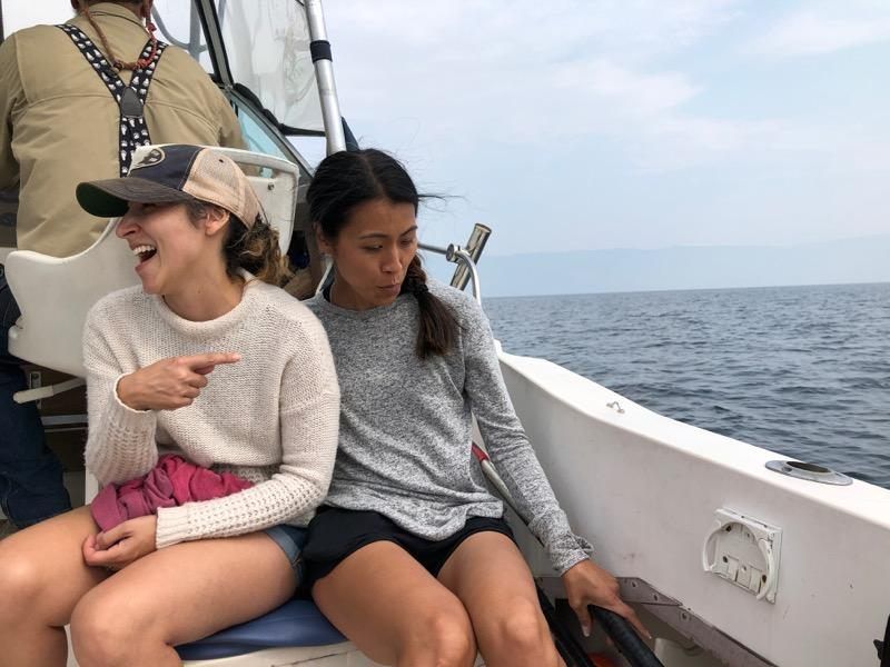 Two women are sitting on a boat laughing and pointing at something.