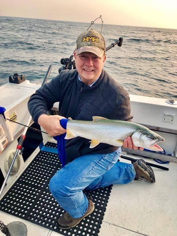 A man is kneeling on a boat holding a large fish
