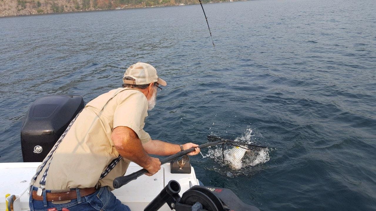 A man is fishing in a boat on a lake.