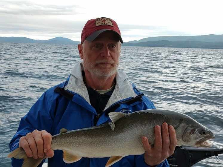 A man is holding a large fish in front of a body of water.