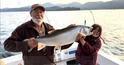 A man and a girl are holding a large fish on a boat.