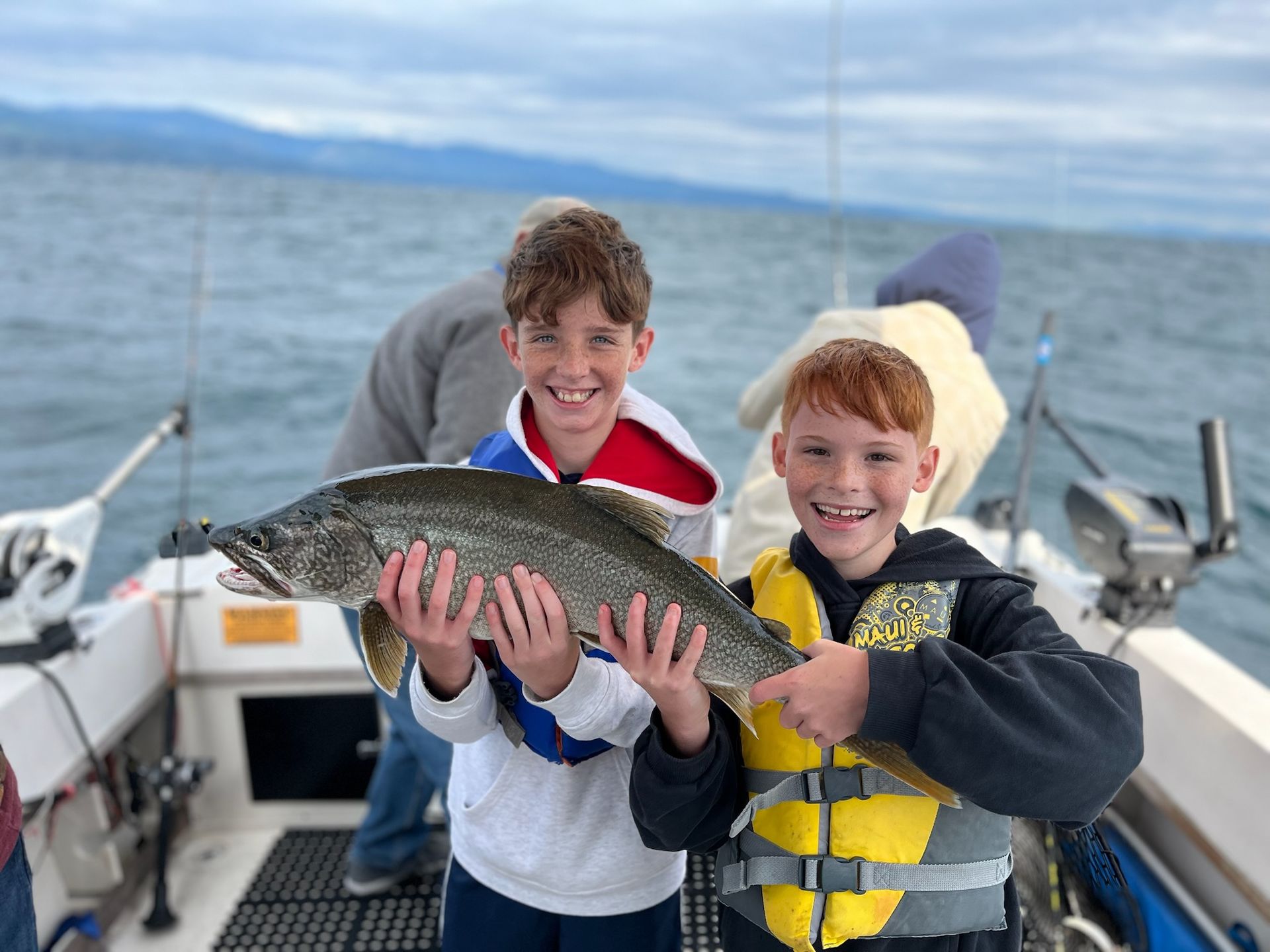 Two young boys are holding a large fish on a boat.