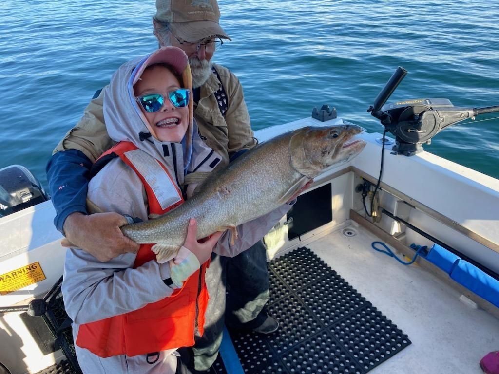 A man and a little girl are holding a large fish on a boat.