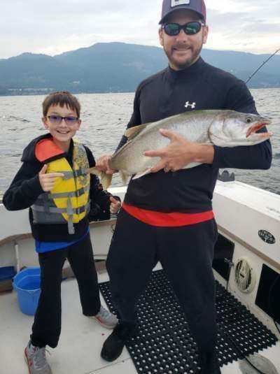 A man and a boy are standing on a boat holding a large fish.