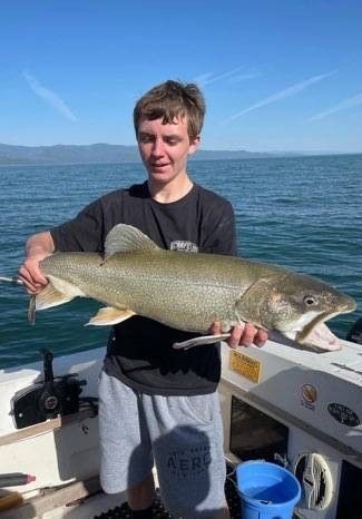 A young man is holding a large fish on a boat.