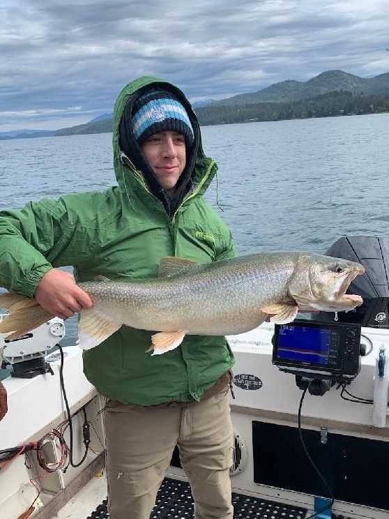 A man in a green jacket is holding a large fish on a boat.
