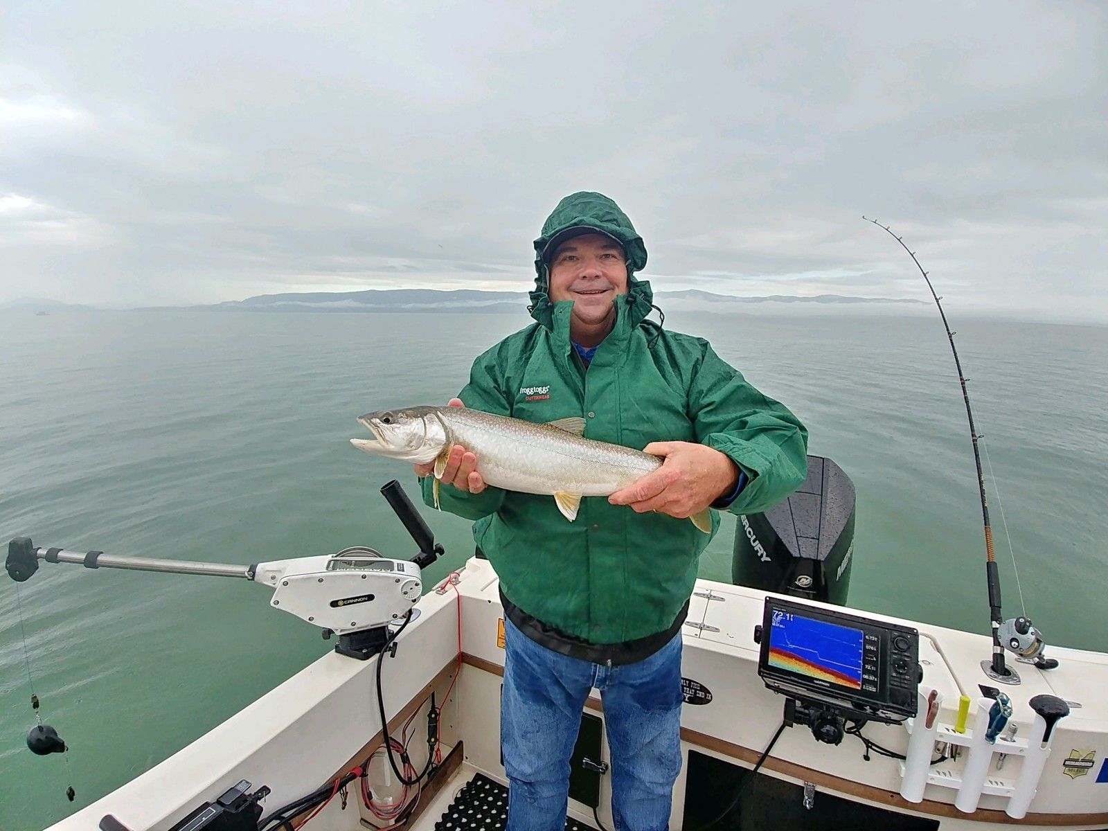 A man in a green jacket is holding a fish on a boat.