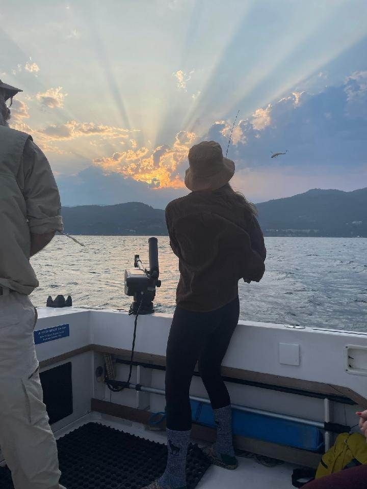 A man and a woman are fishing on a boat at sunset.