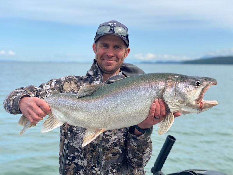 A man is holding a large fish in his hands in front of a body of water.