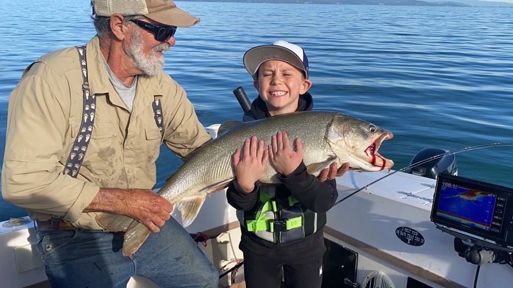 A man and a boy are holding a large fish on a boat.