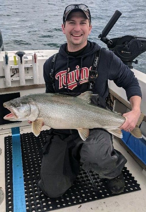 A man is kneeling on a boat holding a large fish.