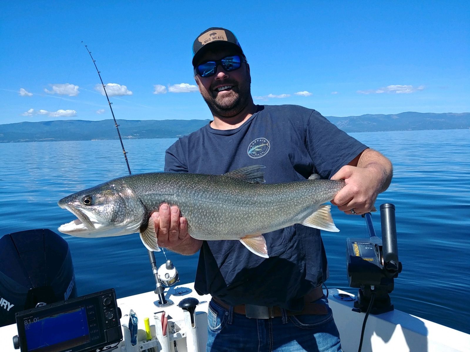 A man is holding a large fish on a boat in the water.