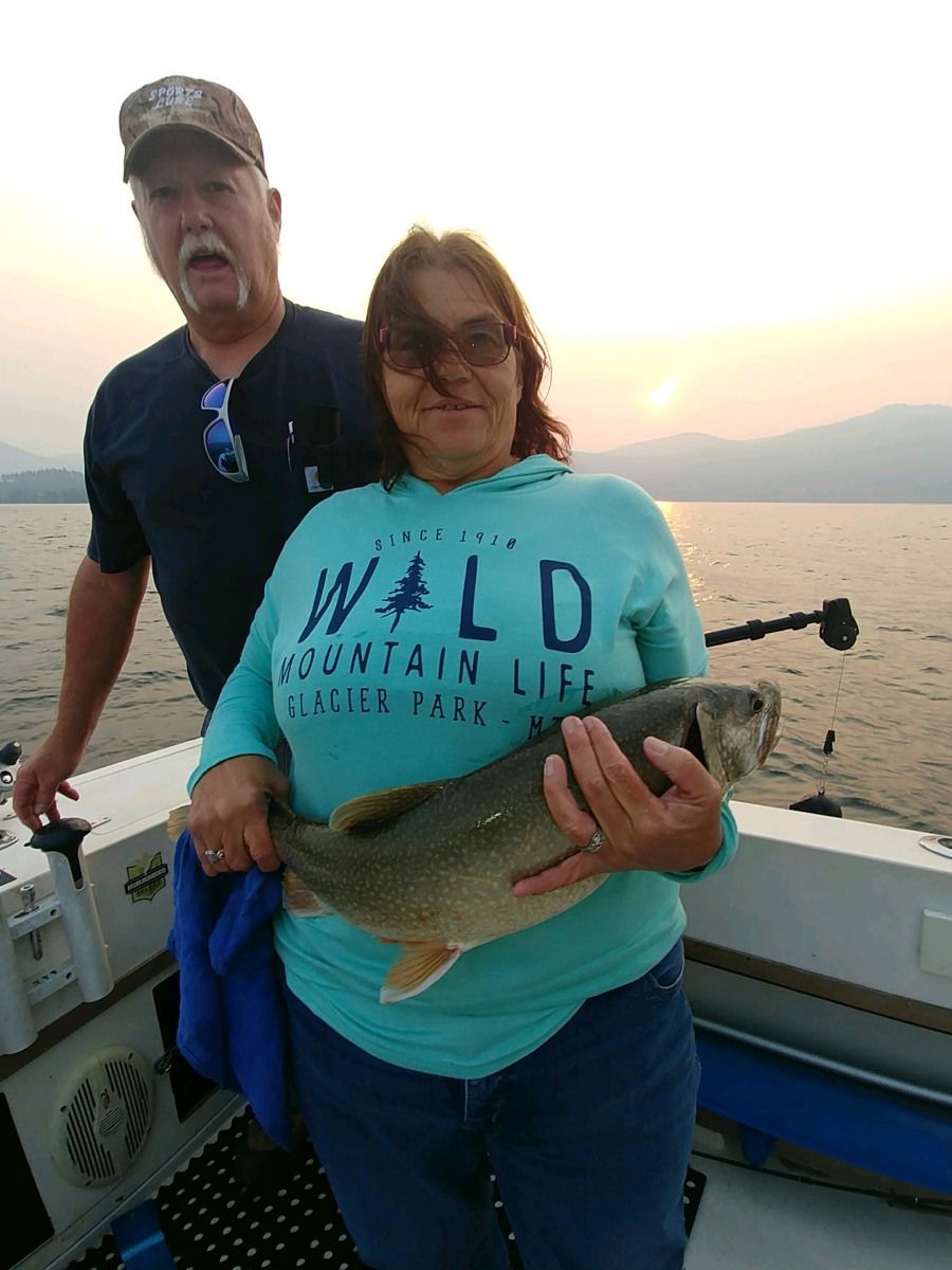 A man and a woman are standing on a boat holding a fish.