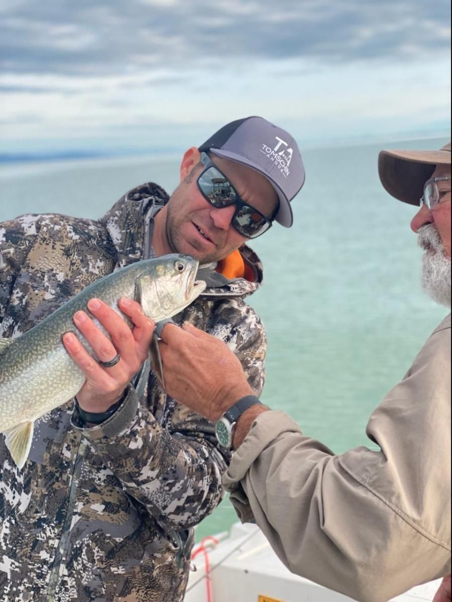 A man wearing a t3 hat is holding a fish