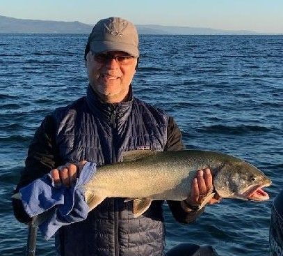 A man is holding a large fish in his hands in front of the ocean.
