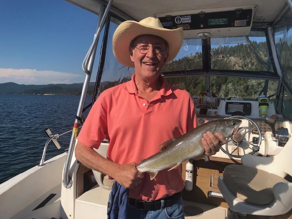 A man in a cowboy hat is holding a fish on a boat.
