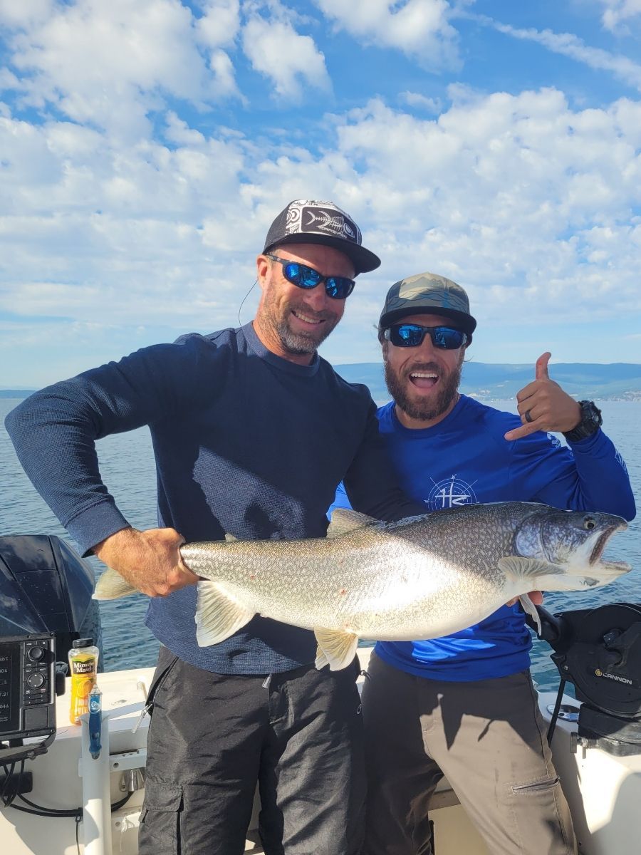 Two men are standing on a boat holding a large fish.